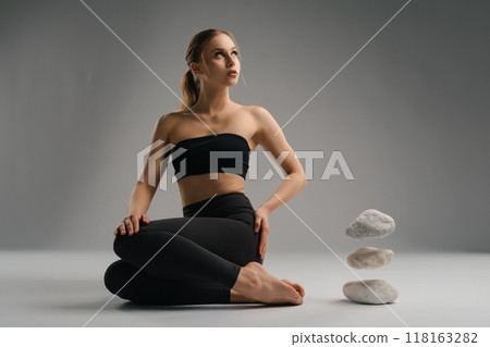 Young woman in yoga pose with stacked stones in minimalist indoor setting Young woman in yoga pose with stacked stones in minimalist indoor setting 118163282