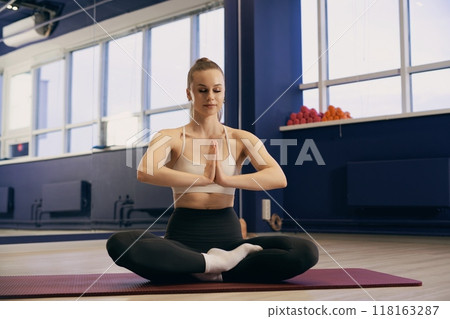 Woman practicing yoga indoors at a modern fitness studio during daylight 118163287