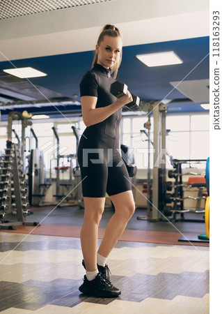Young woman exercises with dumbbell in fitness gym during daytime Young woman exercises with dumbbell in fitness gym during daytime 118163293