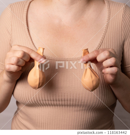 A woman holds deflated balloons, concept of breast modification after feeding a baby, reaching age A woman holds deflated balloons, concept of breast modification after feeding a baby, reaching age 118163442