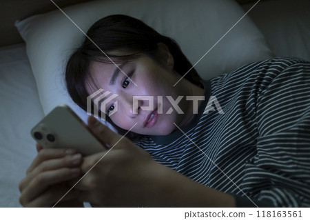 A woman watching a smartphone in bed A woman watching a smartphone in bed 118163561