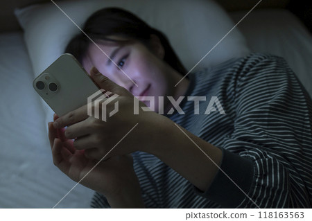 一名婦女在床上的看一個智能手機 118163563