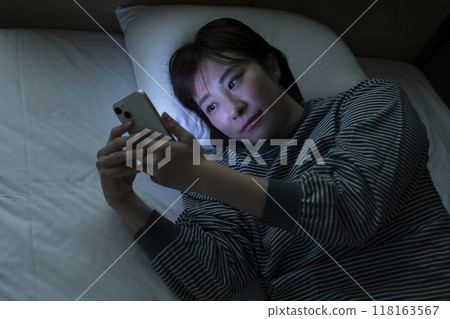 A woman watching a smartphone in bed A woman watching a smartphone in bed 118163567