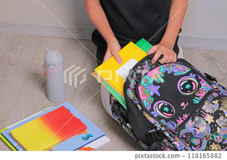 Schoolgirl in uniform black dress sits on floor and pick up school bag. Copy space, background for design, text. Back to school. Schoolgirl in uniform black dress sits on floor and pick up school bag. Copy space, background for design, text. Back to school. 118165882
