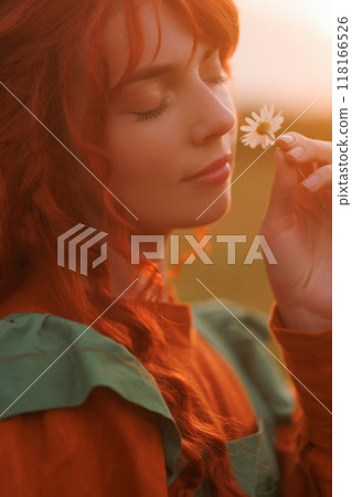 A shepherdess woman with red hair and a green dress in a field on sunset. 118166526