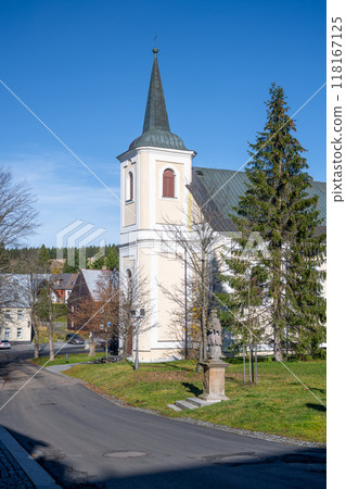 Saint Anne Church stands proudly in Bozi Dar, surrounded by trees and quaint buildings under a clear blue sky. Visitors can appreciate its architecture and the serene atmosphere of the Ore Mountains. 118167125
