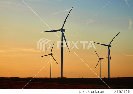 Silhouetted wind turbines in countryside landscape during sunset. Wind power plant generating clean energy. Concept of renewable and sustainable energy 118167146