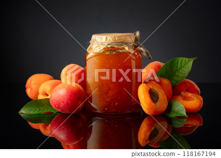 Apricot jam in glass jar and fresh fruits on a black reflective background. Apricot jam in glass jar and fresh fruits on a black reflective background. 118167194