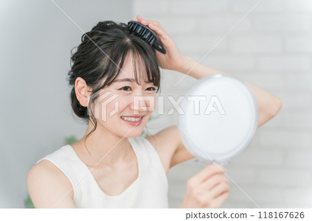Asian woman doing a scalp massage while looking in the mirror Asian woman doing a scalp massage while looking in the mirror 118167626