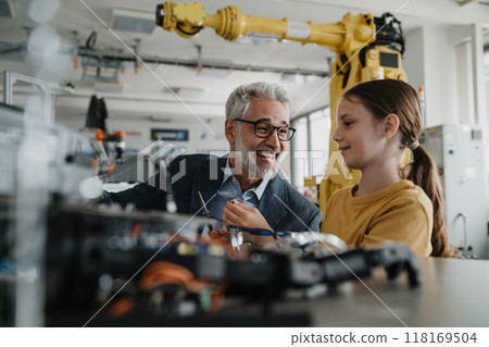 Father and girl during kid at work day, encouraging girl in career in robotics. Teacher showing young schoolgirl how to assemble small robot. 118169504