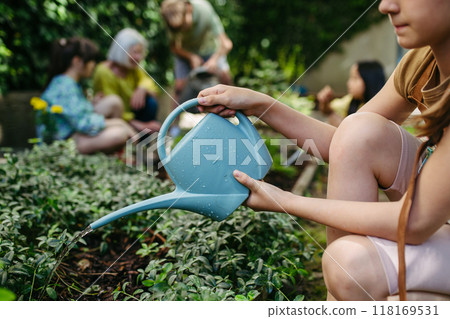 Schoolgirl watering plants in school garden during at outdoor sustainable education class. Concept of experiential learning and ecoliteracy. 118169531
