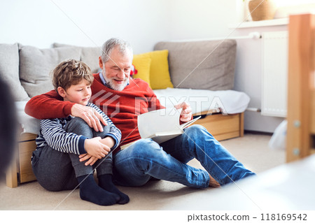 Grandfather spending time with grandson, reading storybook together, sitting on carpet. Grandfather spending time with grandson, reading storybook together, sitting on carpet. 118169542