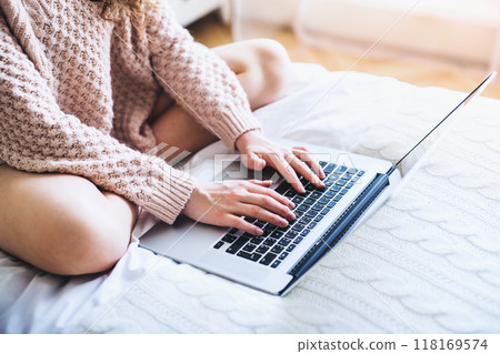 University student writing her thesis on a laptop, sitting at bed in dorm room. 118169574
