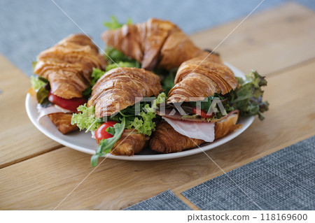Tasty croissants with ham, cheese, salad, tomato and other healthy ingredients. French breakfast for four person. Plate with food on wooden table 118169600