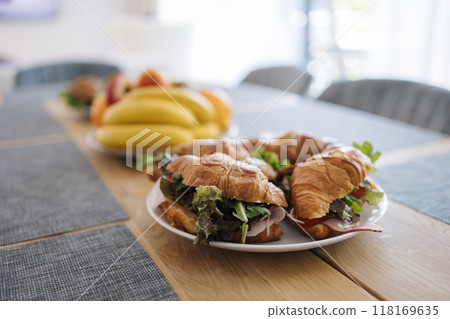 Tasty croissants with ham, cheese, salad, tomato and other healthy ingredients. French breakfast for four person. Plate with food on wooden table 118169635