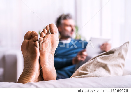 Man at home, watching tv show on tablet, sitting on sofa with feet up. Focus on feet. 118169676