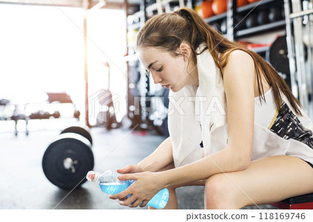 Young fitness girl drinking blue sport drink after hard workout in gym, side view. 118169746