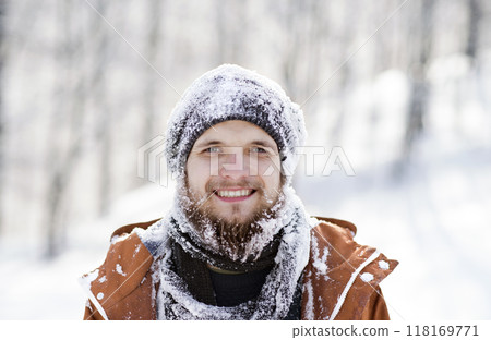 Portrait of young man in the snowy nature, snow stuck to clothes and beard. First snowfall of the season. 118169771