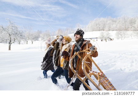 Group of friends pulling sleds behind them, going to sleddingin in snowy nature. First snowfall of the season. Group of friends pulling sleds behind them, going to sleddingin in snowy nature. First snowfall of the season. 118169777