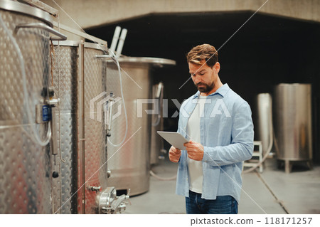 The winemaker standing in the wine cellar, monitoring the fermentation and aging processes in large barrels. The winemaker standing in the wine cellar, monitoring the fermentation and aging processes in large barrels. 118171257