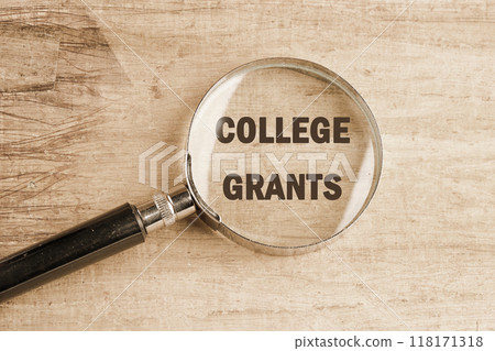 Business and COLLEGE GRANTS concept. Copy space. Grant symbol COLLEGE GRANTS through a magnifying glass on papyrus. View from above. 118171318