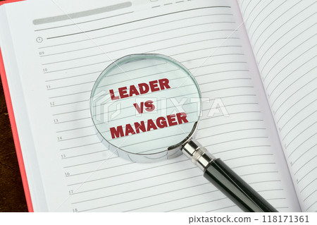 Leader vs manager is shown through a magnifying glass on a blank page of a notebook, a book 118171361