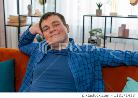 Happy Caucasian man entering home room sits on orange sofa relaxing resting dreaming taking a break Happy Caucasian man entering home room sits on orange sofa relaxing resting dreaming taking a break 118171438