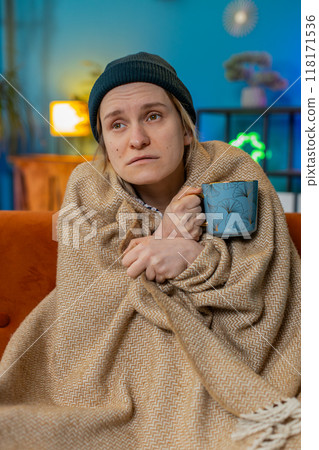 Ill sick unhealthy woman freezes from the cold feels bad covered by warm blanket drinks tea at home 118171536