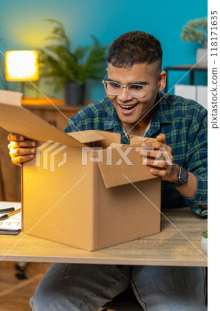 Happy man shopper unpacking cardboard box delivery parcel online shopping purchase at home office 118171635