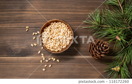Pine nuts in a bowl on a brown wooden background with a branch of pine needles. Healthy diet snack. Pine nuts in a bowl on a brown wooden background with a branch of pine needles. Healthy diet snack. 118172260