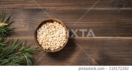 Pine nuts in a bowl on a brown wooden background with a branch of pine needles. Healthy diet snack. Pine nuts in a bowl on a brown wooden background with a branch of pine needles. Healthy diet snack. 118172262