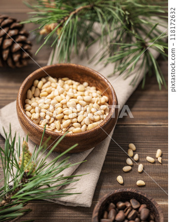 Pine nuts in a bowl on napkin and a handful of unpeeled nuts on a brown wooden background Pine nuts in a bowl on napkin and a handful of unpeeled nuts on a brown wooden background 118172632