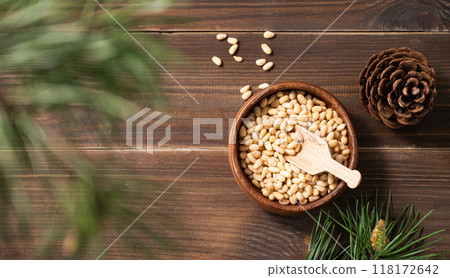 Pine nuts in a bowl on a dark wooden background with branches of pine needles and cone. Pine nuts in a bowl on a dark wooden background with branches of pine needles and cone. 118172642