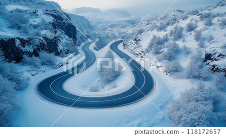 A drone photograph of a winding mountain road during winter, with snow foliage and dramatic landscapes 118172657