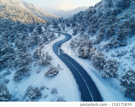 A drone photograph of a winding mountain road during winter, with snow foliage and dramatic landscapes 118172659