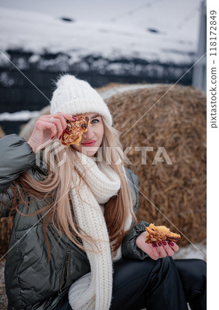 Woman enjoying a cookie outdoors near hay bales in a snowy landscape during wintertime 118172849