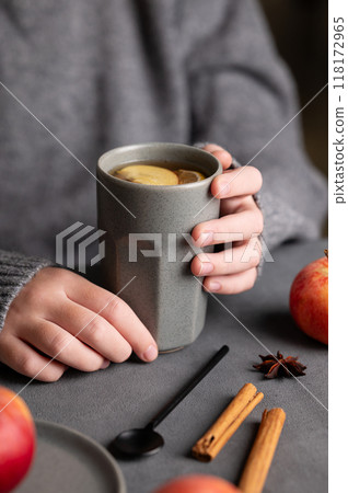 Hands hold a gray glass with homemade apple punch or cider with apples and cinnamon Hands hold a gray glass with homemade apple punch or cider with apples and cinnamon 118172965