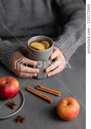 Hands hold a gray glass with homemade apple punch or cider with apples and cinnamon  118172969