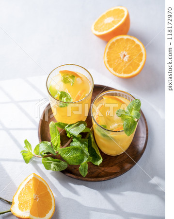 Freshly squeezed juice in a glass with fresh oranges, mint and ice on a light background with shadow 118172970