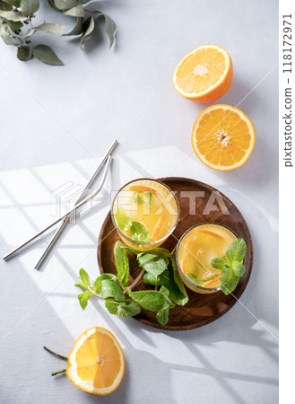 Freshly squeezed juice in a glass with fresh oranges, mint and ice on a light background  118172971