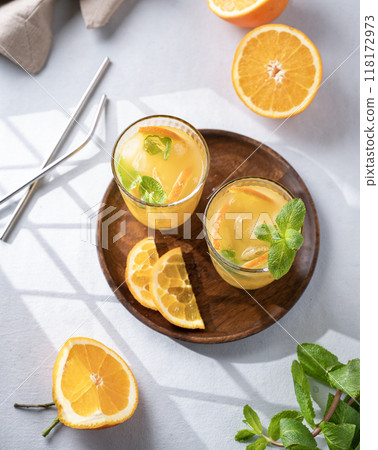 Freshly squeezed juice in a glass with fresh oranges, mint and ice on a light background  118172973
