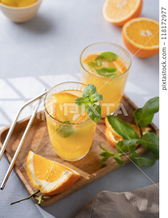 Freshly squeezed juice in a glass with fresh oranges, mint and ice on a light background 118172977