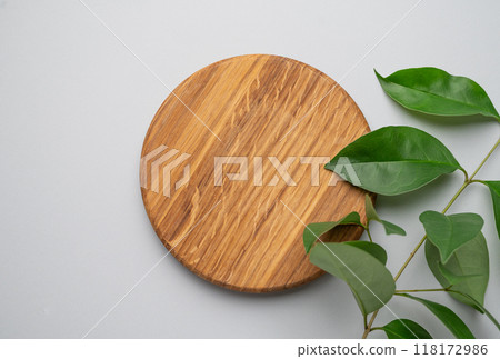 Modern empty product display. Minimal wooden round board with green leaves on a gray background. 118172986