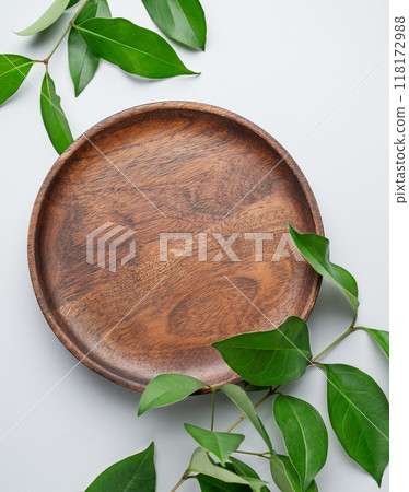 Modern empty product display. Minimal wooden round plate with green leaves on a gray background 118172988