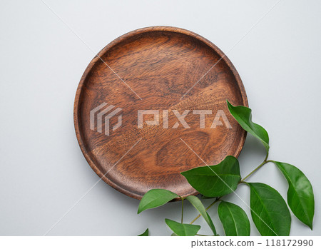 Modern empty product display. Minimal wooden round plate with green leaves on a gray background. Modern empty product display. Minimal wooden round plate with green leaves on a gray background. 118172990