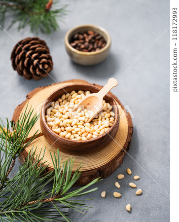 Pine nuts in a bowl on a blue background with branches of pine needles and cone. Pine nuts in a bowl on a blue background with branches of pine needles and cone. 118172993