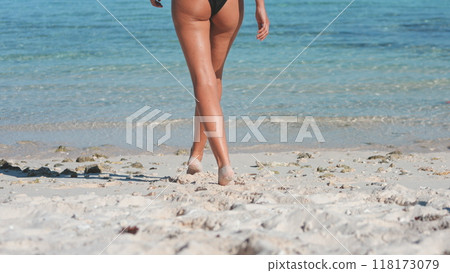 Woman is walking away from the camera on a white sand beach leaving footprints in the sand, enjoying a sunny vacation day 118173079