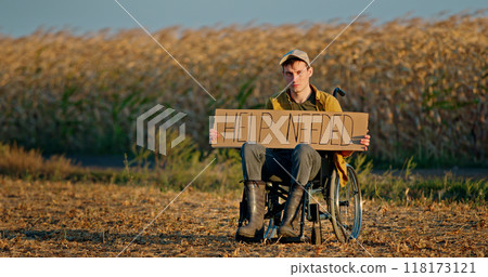 A man in a wheelchair holding a HELP NEEDED sign in a dry field at sunset. A man in a wheelchair holding a HELP NEEDED sign in a dry field at sunset. 118173121