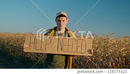 A man farmer standing in a field holding a cardboard sign that reads HELP NEEDED. A man farmer standing in a field holding a cardboard sign that reads HELP NEEDED. 118173123