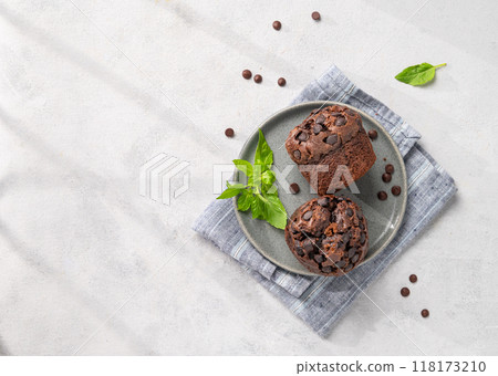 Chocolate muffins on a plate with mint on a light background with morning shadow.  118173210